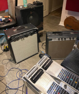 Several pieces of gear including a Standel combo amplifier, a speaker cabinet, a TONEX pedal, and an Emmons D10